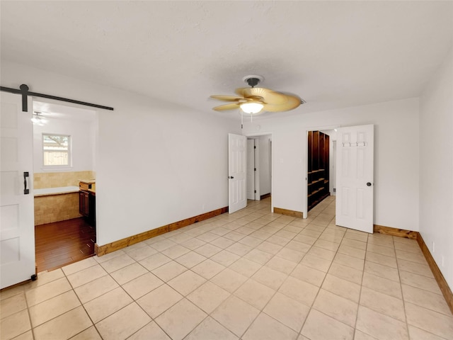 unfurnished bedroom with connected bathroom, ceiling fan, a barn door, and light tile patterned flooring