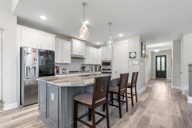 kitchen featuring stainless steel appliances, light stone counters, a breakfast bar, white cabinets, and a center island with sink