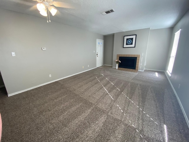 unfurnished living room featuring ceiling fan, a fireplace, dark carpet, and a textured ceiling