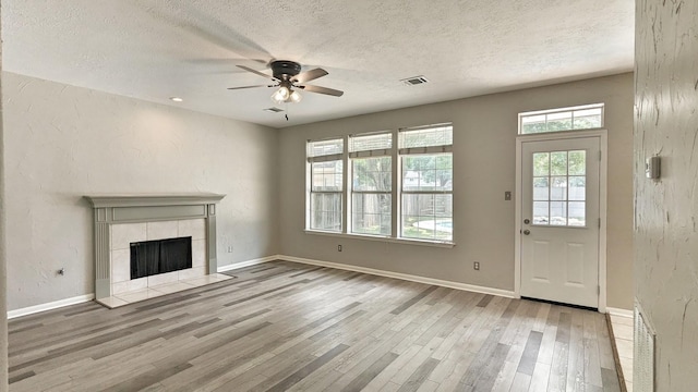 unfurnished living room featuring a textured ceiling, ceiling fan, light hardwood / wood-style flooring, and a tiled fireplace