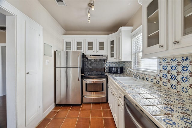 kitchen with decorative backsplash, appliances with stainless steel finishes, sink, dark tile patterned flooring, and white cabinetry