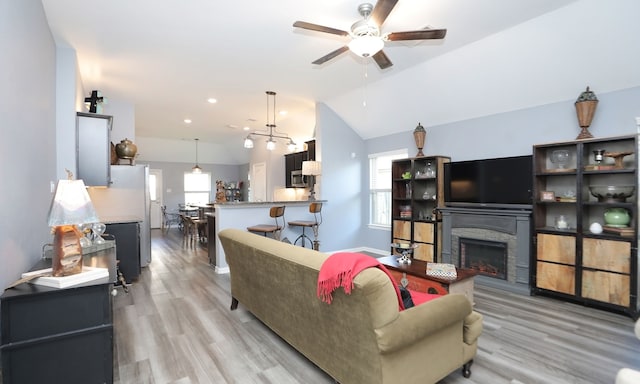 living room featuring ceiling fan, a fireplace, light hardwood / wood-style floors, and vaulted ceiling