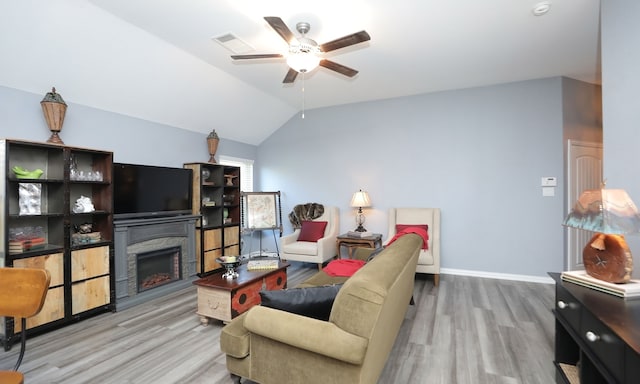 living room featuring ceiling fan, a stone fireplace, wood-type flooring, and vaulted ceiling