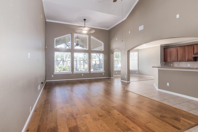 unfurnished living room with light wood-type flooring, high vaulted ceiling, ceiling fan, and ornamental molding