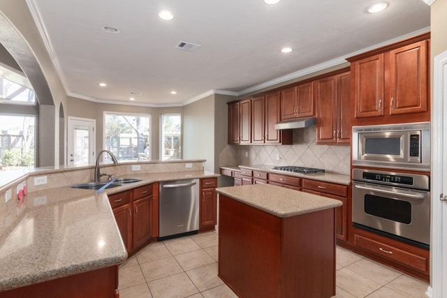 kitchen with backsplash, sink, ornamental molding, appliances with stainless steel finishes, and a kitchen island