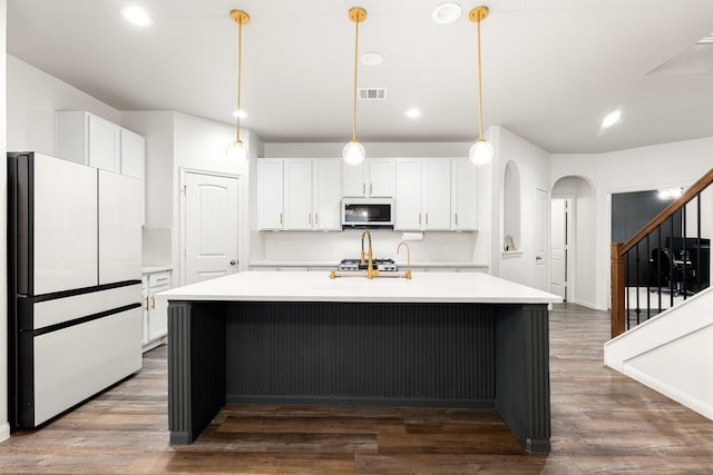 kitchen featuring white cabinets, decorative light fixtures, a center island with sink, and white appliances