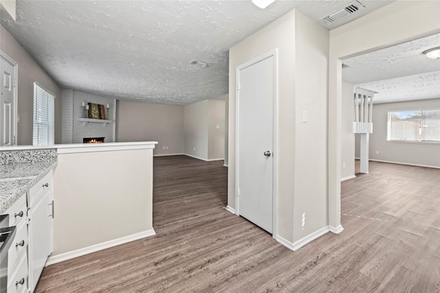 kitchen featuring a large fireplace, white cabinets, a textured ceiling, and hardwood / wood-style flooring