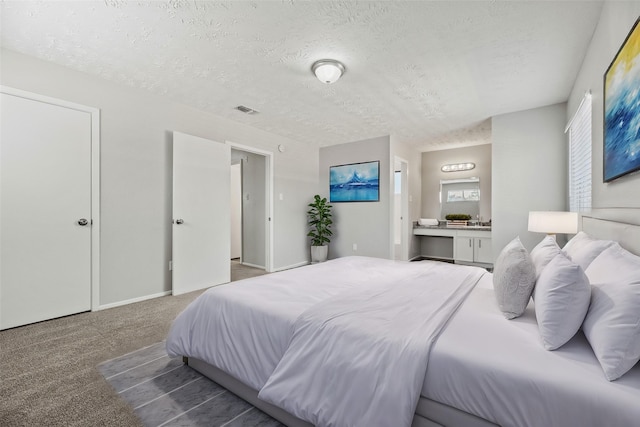 bedroom featuring carpet, ensuite bathroom, and a textured ceiling