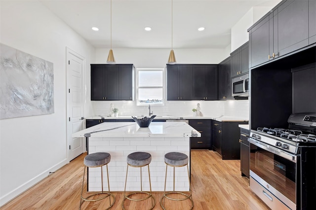 kitchen with light stone countertops, pendant lighting, stainless steel appliances, and light hardwood / wood-style flooring