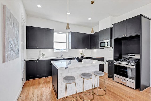 kitchen featuring a center island, sink, appliances with stainless steel finishes, decorative light fixtures, and light hardwood / wood-style floors