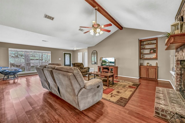 living room featuring vaulted ceiling with beams, ceiling fan, hardwood / wood-style floors, and a brick fireplace