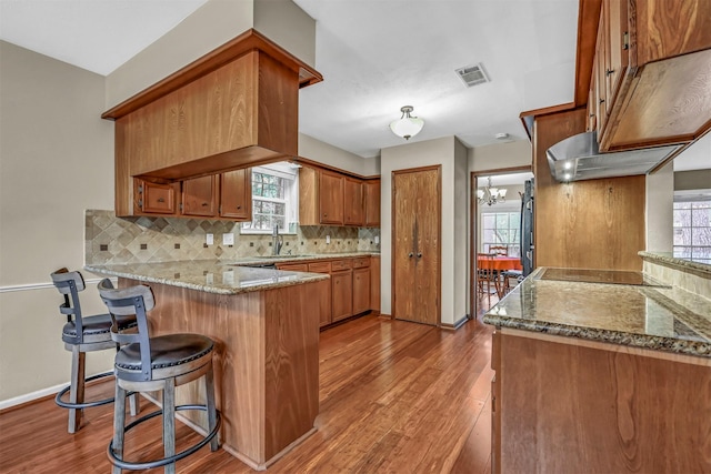 kitchen featuring kitchen peninsula, decorative backsplash, light stone countertops, light hardwood / wood-style flooring, and a notable chandelier