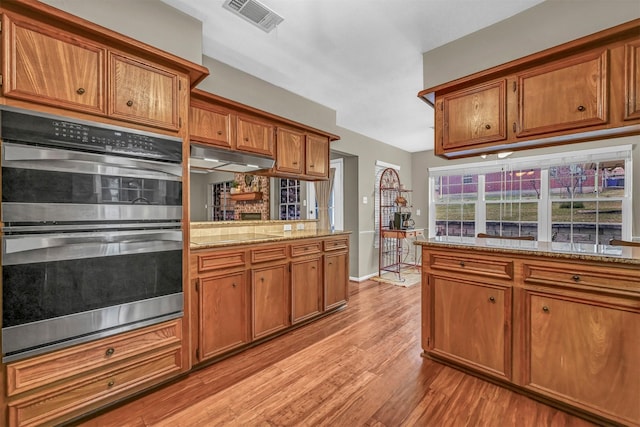 kitchen with light stone countertops, stainless steel double oven, kitchen peninsula, and light hardwood / wood-style flooring