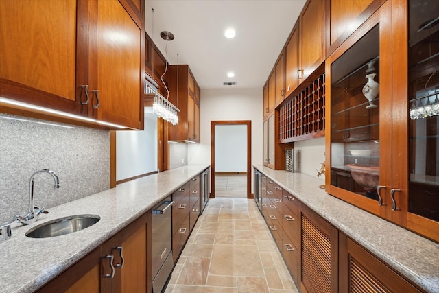 kitchen with pendant lighting, dishwasher, sink, tasteful backsplash, and light stone counters