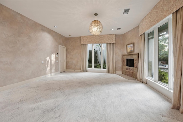 unfurnished living room with a premium fireplace, carpet floors, a wealth of natural light, and an inviting chandelier