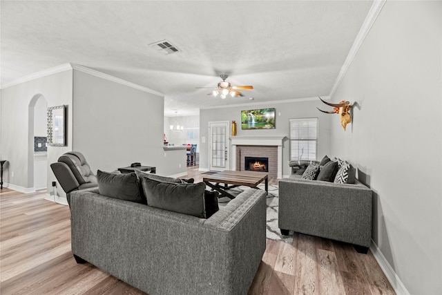 living room featuring ceiling fan, hardwood / wood-style floors, crown molding, and a brick fireplace