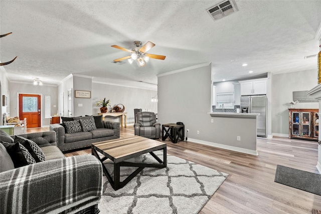 living room with a textured ceiling, light hardwood / wood-style flooring, ceiling fan, and crown molding