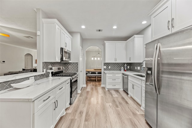 kitchen with light stone counters, ornamental molding, stainless steel appliances, white cabinets, and light hardwood / wood-style floors