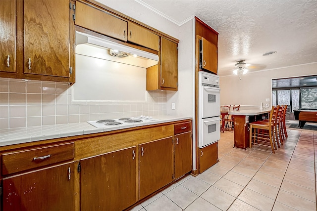 kitchen with visible vents, light tile patterned flooring, a textured ceiling, white appliances, and under cabinet range hood