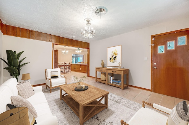 living area featuring light tile patterned floors, a textured ceiling, a notable chandelier, visible vents, and baseboards