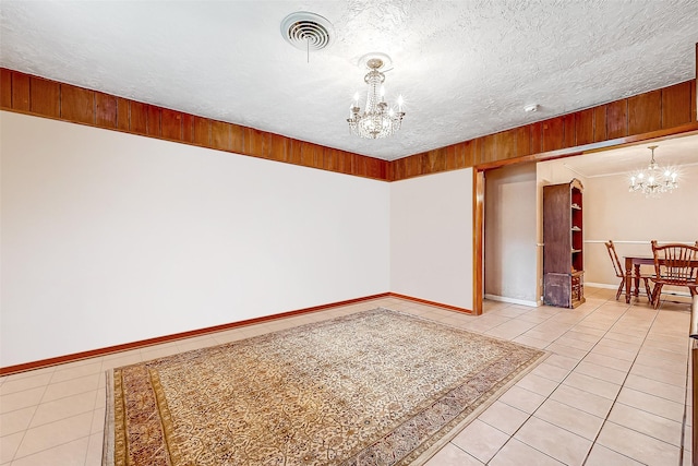 tiled empty room featuring a textured ceiling and a chandelier