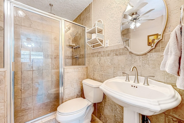 bathroom with sink, a shower with door, tile walls, a textured ceiling, and toilet