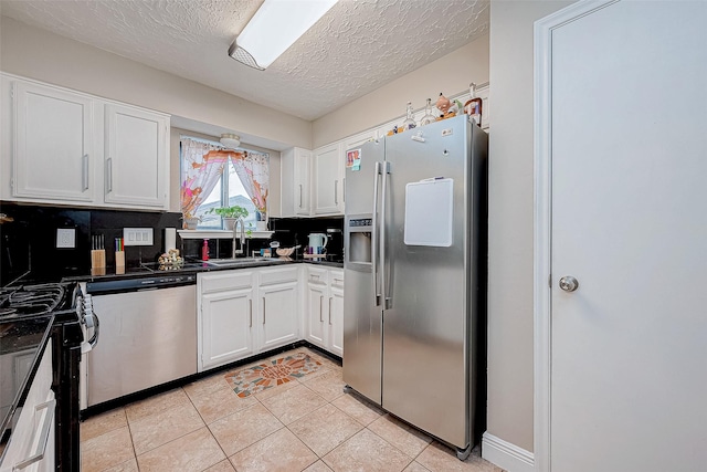 kitchen with appliances with stainless steel finishes, tasteful backsplash, sink, white cabinetry, and light tile patterned flooring