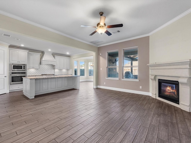 kitchen with custom exhaust hood, decorative backsplash, an island with sink, white cabinetry, and stainless steel appliances