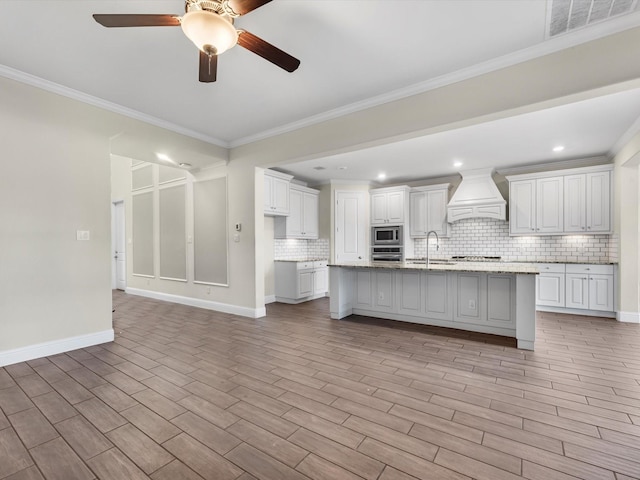 kitchen featuring white cabinets, a center island with sink, tasteful backsplash, and custom exhaust hood