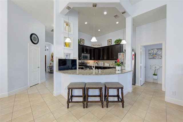 kitchen with appliances with stainless steel finishes, light tile patterned floors, light stone counters, and a high ceiling