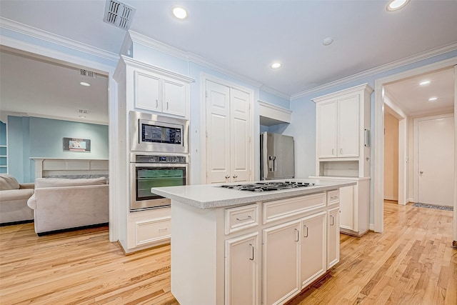 kitchen featuring light wood-type flooring, stainless steel appliances, crown molding, a center island, and white cabinetry