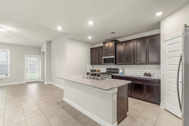 kitchen with sink, an island with sink, light tile patterned flooring, light stone counters, and stainless steel appliances