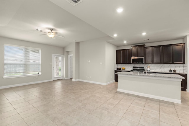 kitchen with tasteful backsplash, an island with sink, dark brown cabinets, light tile patterned floors, and appliances with stainless steel finishes