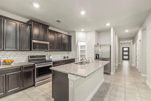 kitchen with a center island with sink, sink, light tile patterned flooring, light stone counters, and stainless steel appliances