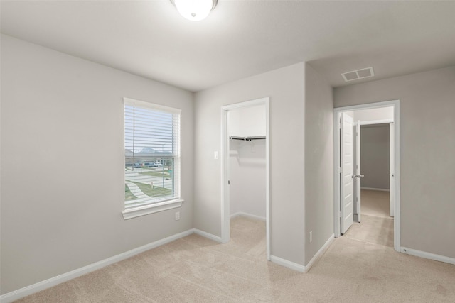 unfurnished bedroom featuring light colored carpet, a walk in closet, and a closet