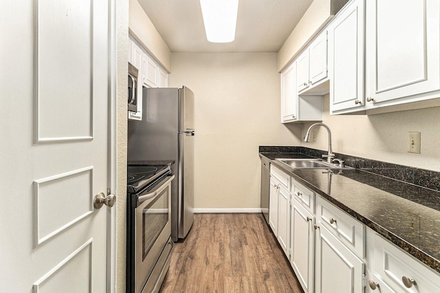 kitchen featuring dark wood-type flooring, sink, dark stone countertops, appliances with stainless steel finishes, and white cabinetry