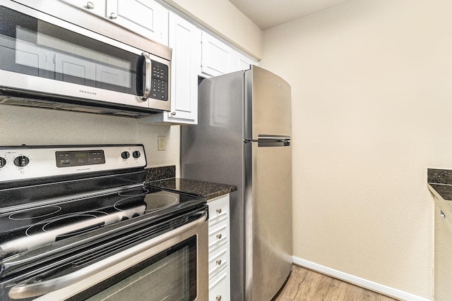 kitchen with white cabinets, appliances with stainless steel finishes, light hardwood / wood-style floors, and dark stone countertops