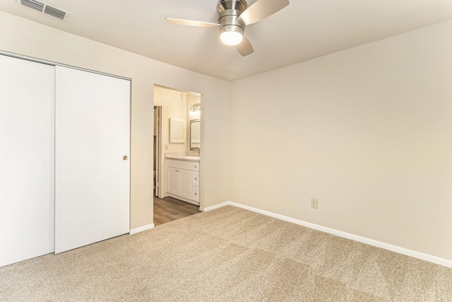 unfurnished bedroom featuring carpet, ceiling fan, sink, connected bathroom, and a closet