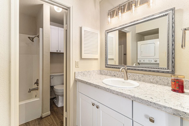 full bathroom with vanity, shower / bathing tub combination, hardwood / wood-style flooring, stacked washer and clothes dryer, and toilet