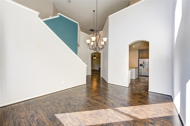 unfurnished room with a high ceiling, ceiling fan with notable chandelier, crown molding, and dark wood-type flooring