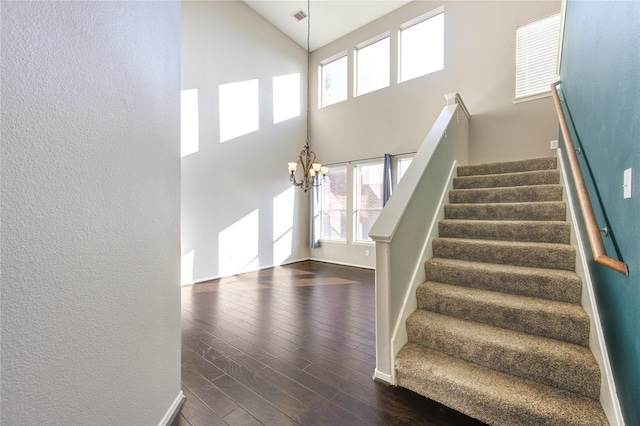 stairway featuring hardwood / wood-style flooring, a towering ceiling, and an inviting chandelier