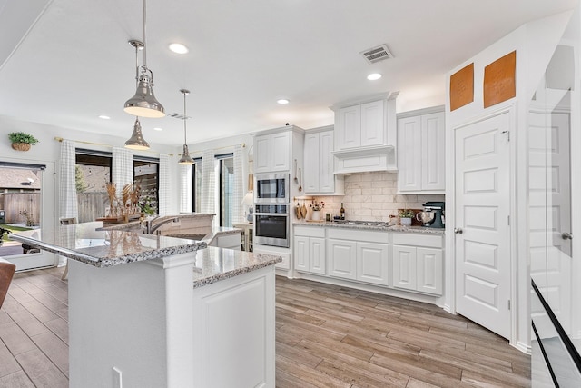 kitchen with light stone countertops, an island with sink, decorative light fixtures, white cabinets, and appliances with stainless steel finishes