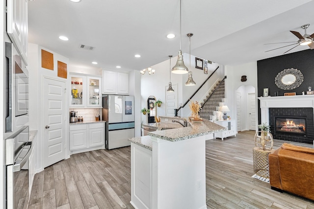 kitchen with backsplash, appliances with stainless steel finishes, decorative light fixtures, light stone counters, and white cabinetry