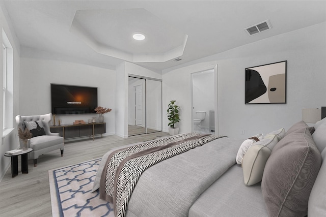 bedroom featuring a raised ceiling, a closet, and light hardwood / wood-style floors