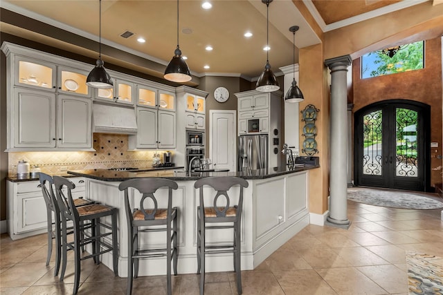 kitchen with ornate columns, range hood, backsplash, stainless steel appliances, and crown molding