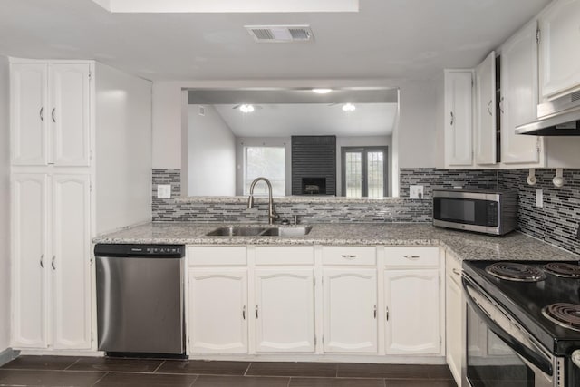 kitchen featuring a large fireplace, ventilation hood, stainless steel appliances, sink, and white cabinets