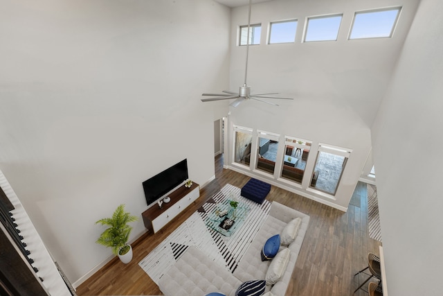 living room featuring hardwood / wood-style floors, ceiling fan, and a towering ceiling