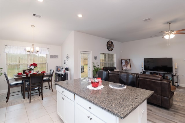 kitchen with ceiling fan with notable chandelier, pendant lighting, stone countertops, white cabinets, and a center island