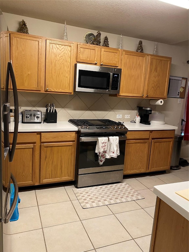 kitchen featuring tasteful backsplash, light tile patterned floors, stainless steel appliances, and a textured ceiling