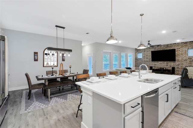 kitchen featuring white cabinets, dishwasher, open floor plan, light wood-style floors, and a sink